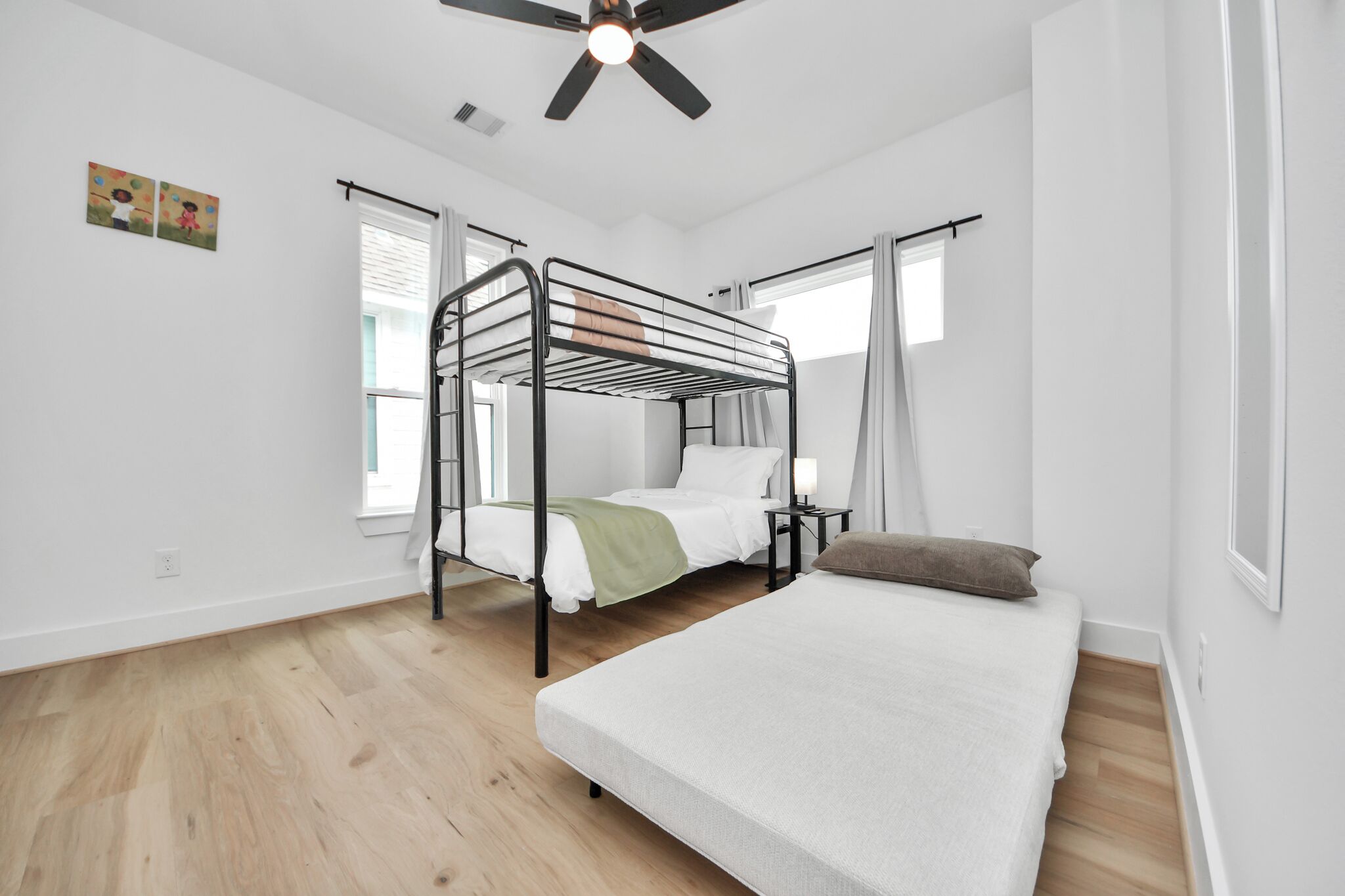 A room with a bunk bed, a single bed, a ceiling fan, and a window with curtains.