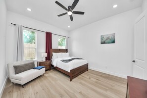 A bedroom with a bed, a nightstand, a lamp, a window with curtains, a ceiling fan, and a painting on the wall. - Château Idaho - Cozy•Sleeps 10•NRG•Med Center•UoH (Houston)