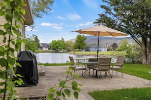 Un patio con tavolo e sedie, un barbecue e vista su un lago e le montagne.