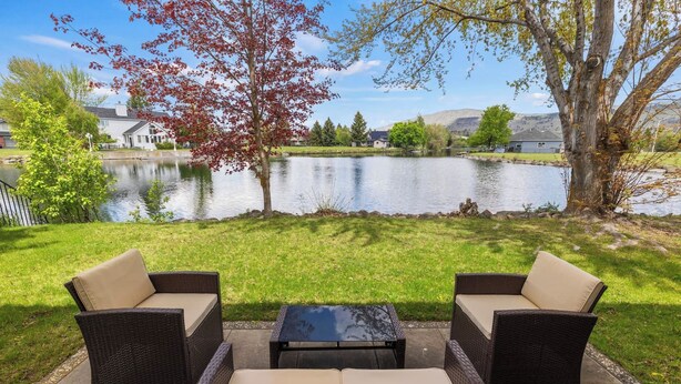 An outdoor seating area with wicker furniture and a glass table, overlooking a lake with houses and trees in the background. - Charter Cove|Fish|Golf|Relax (Klamath Falls)