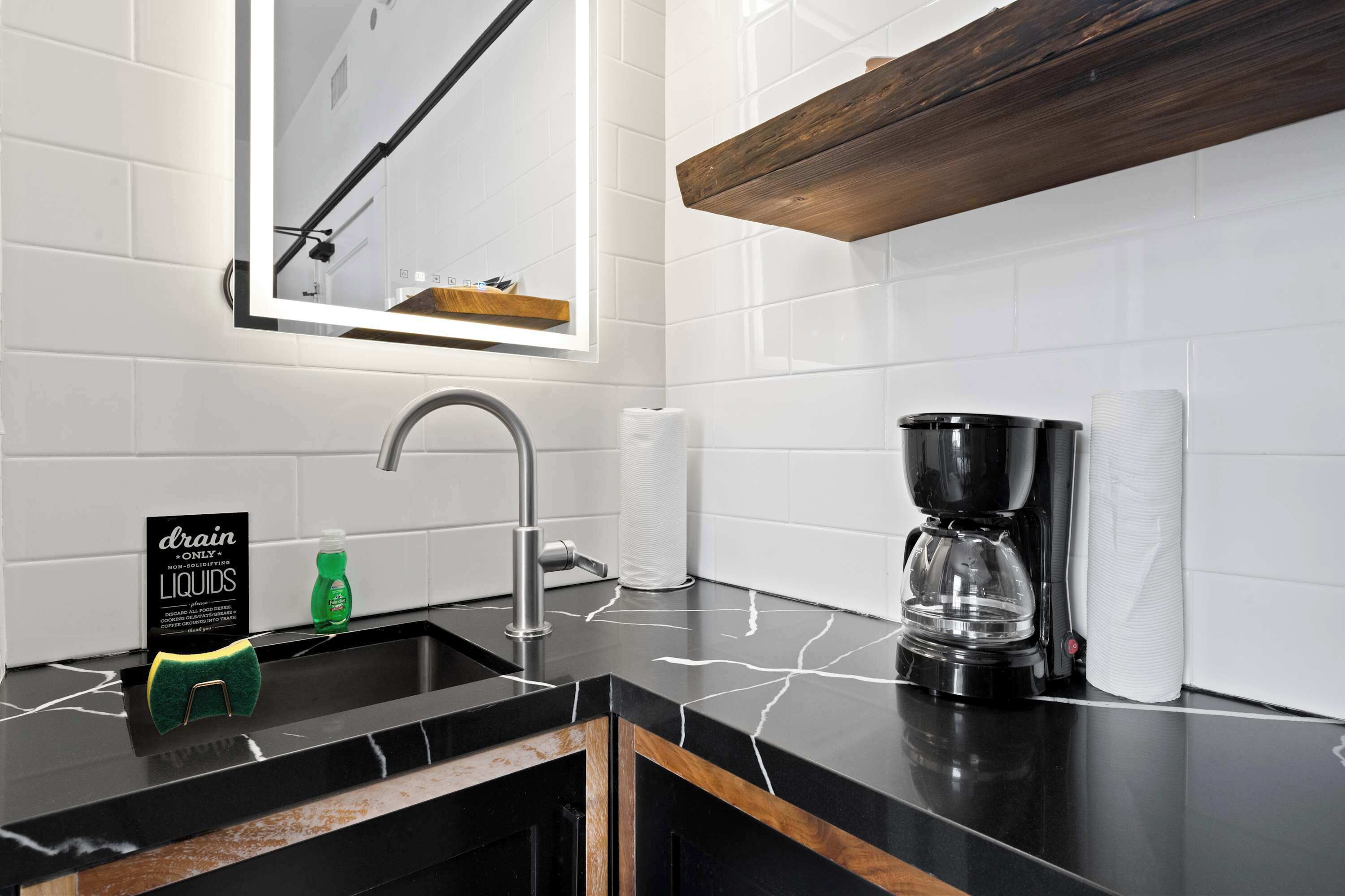 A modern kitchen with a black countertop, a coffee maker, a sink, and a mirror above the sink.