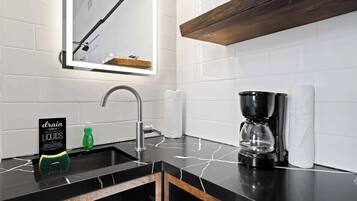 A modern kitchen with a black countertop, a coffee maker, a sink, and a mirror above the sink.