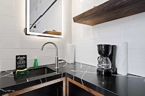 A modern kitchen with a black countertop, a coffee maker, a sink, and a mirror above the sink. - La Ventana Hotel - Renovated Room Steps from Gaslamp Quarter (San Diego)