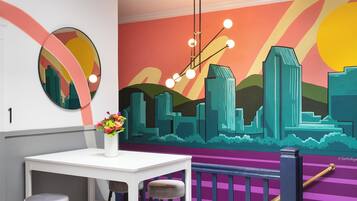 A modern interior with a white table, two bar stools, a vase with flowers, and a colorful mural on the wall.