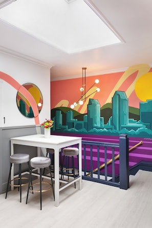 A modern interior with a white table, two bar stools, a vase with flowers, and a colorful mural on the wall. - La Ventana Hotel - Renovated Room Steps from Gaslamp Quarter (San Diego)