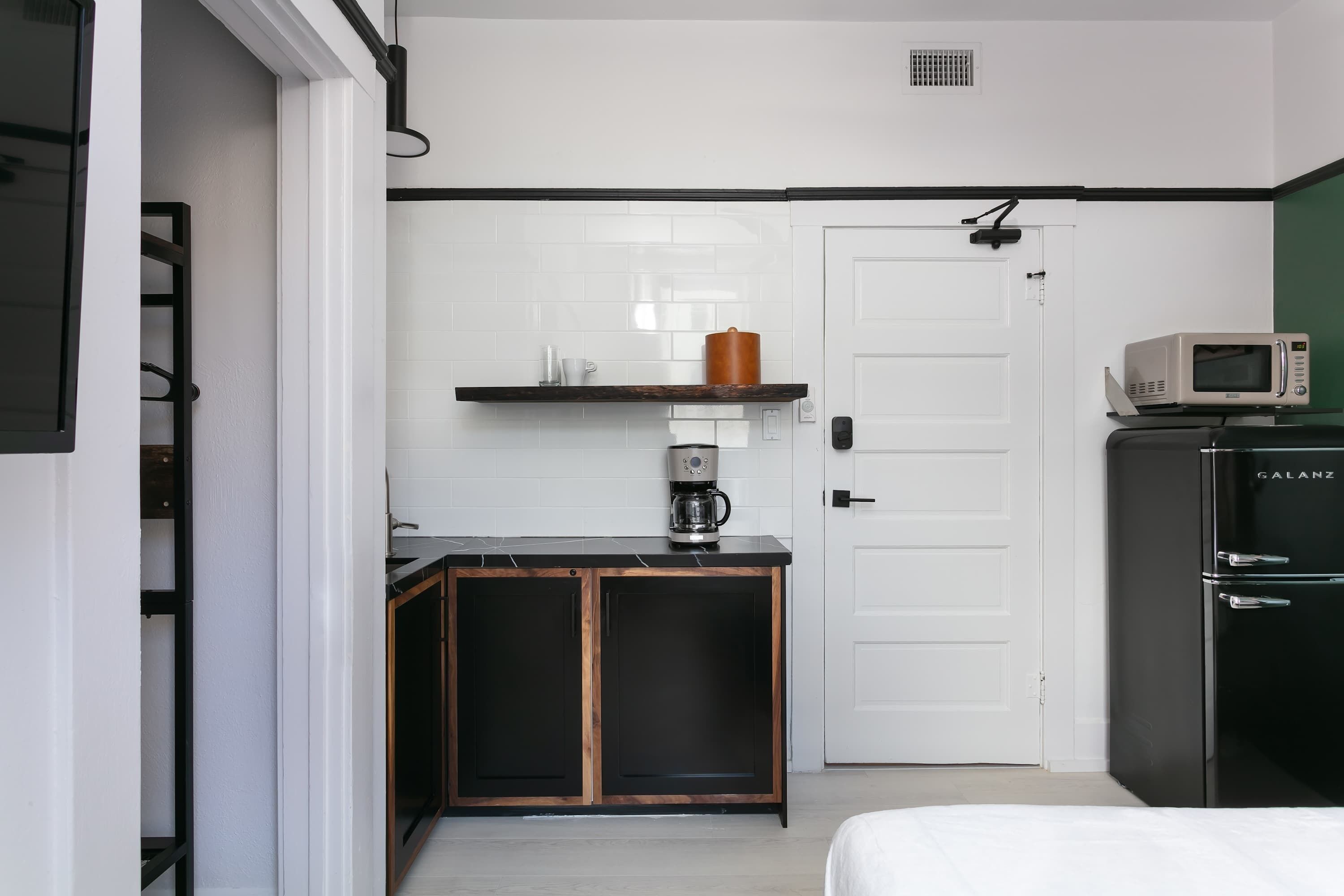 A compact kitchen with a microwave, a coffee maker, and a shelf with a mug and a container.
