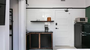 A compact kitchen with a microwave, a coffee maker, and a shelf with a mug and a container.