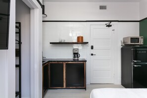 A compact kitchen with a microwave, a coffee maker, and a shelf with a mug and a container. - La Ventana Hotel - Renovated Room Steps from Gaslamp Quarter (San Diego)