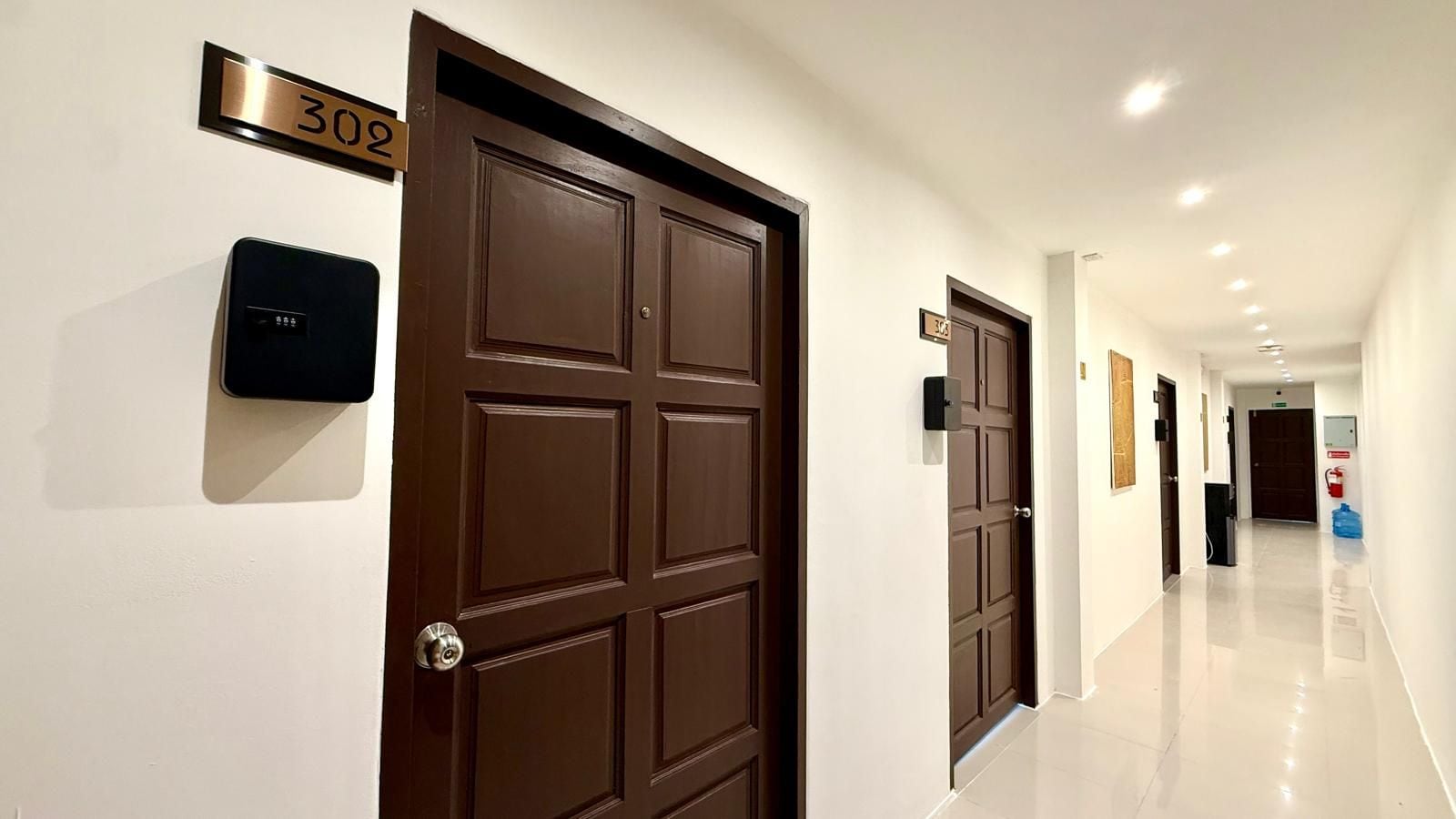 A hotel hallway with a brown door marked '302', a fire extinguisher, and a clean, shiny floor.
