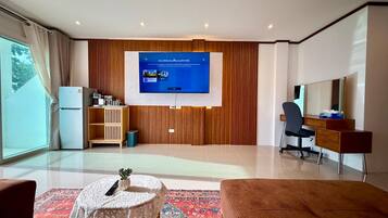 Una sala moderna con televisor de pantalla plana, un mueble de madera, un escritorio con silla y un ventanal grande.