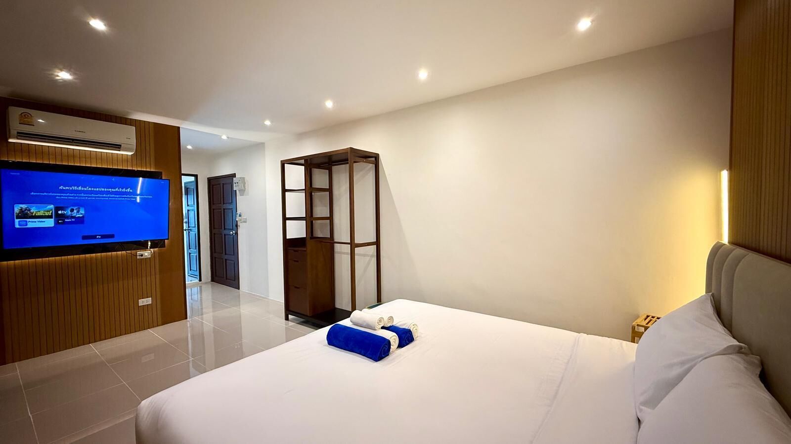 Una habitación de hotel moderna con una cama grande, un televisor montado en la pared y un armario de madera.