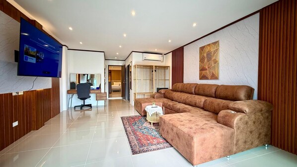 Ein modernes Wohnzimmer mit einem großen braunen Sofa, einem flachbildfernseher an der Wand und einem kleinen Tisch mit einem dekorativen Gegenstand.