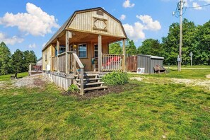 A wooden barn-style building with a porch, a small shed, and a grassy yard.