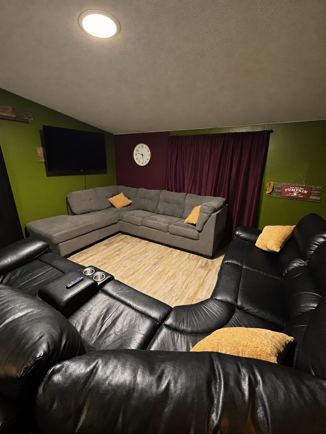 Un salon comprenant un canapé d’angle, un téléviseur à écran plat, une horloge et un panneau décoratif au mur.