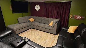 Un salon comprenant un canapé d’angle, un téléviseur à écran plat, une horloge et un panneau décoratif au mur.