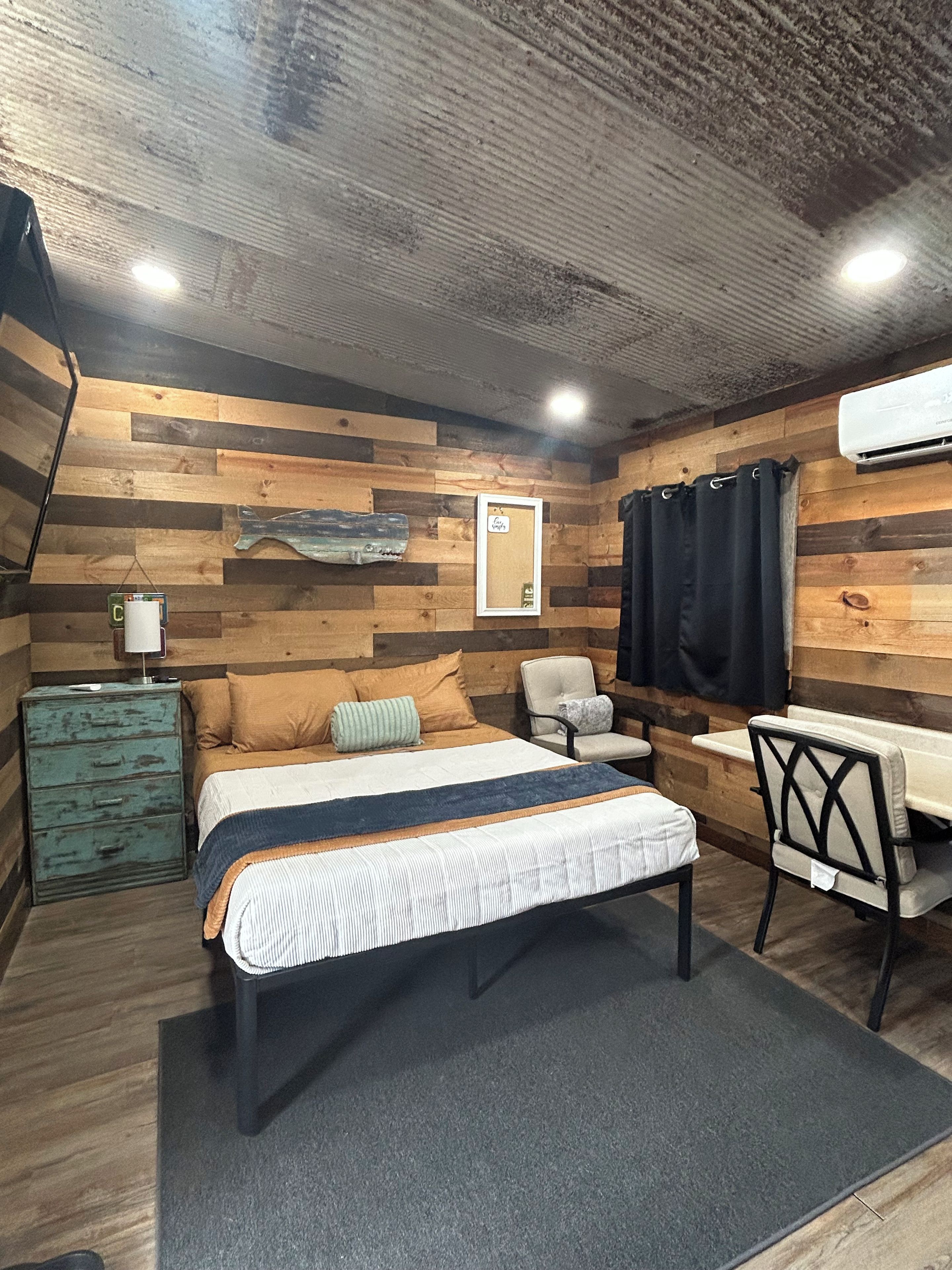 Quarto com cama, cadeira, penteadeira e ar-condicionado fixado na parede.