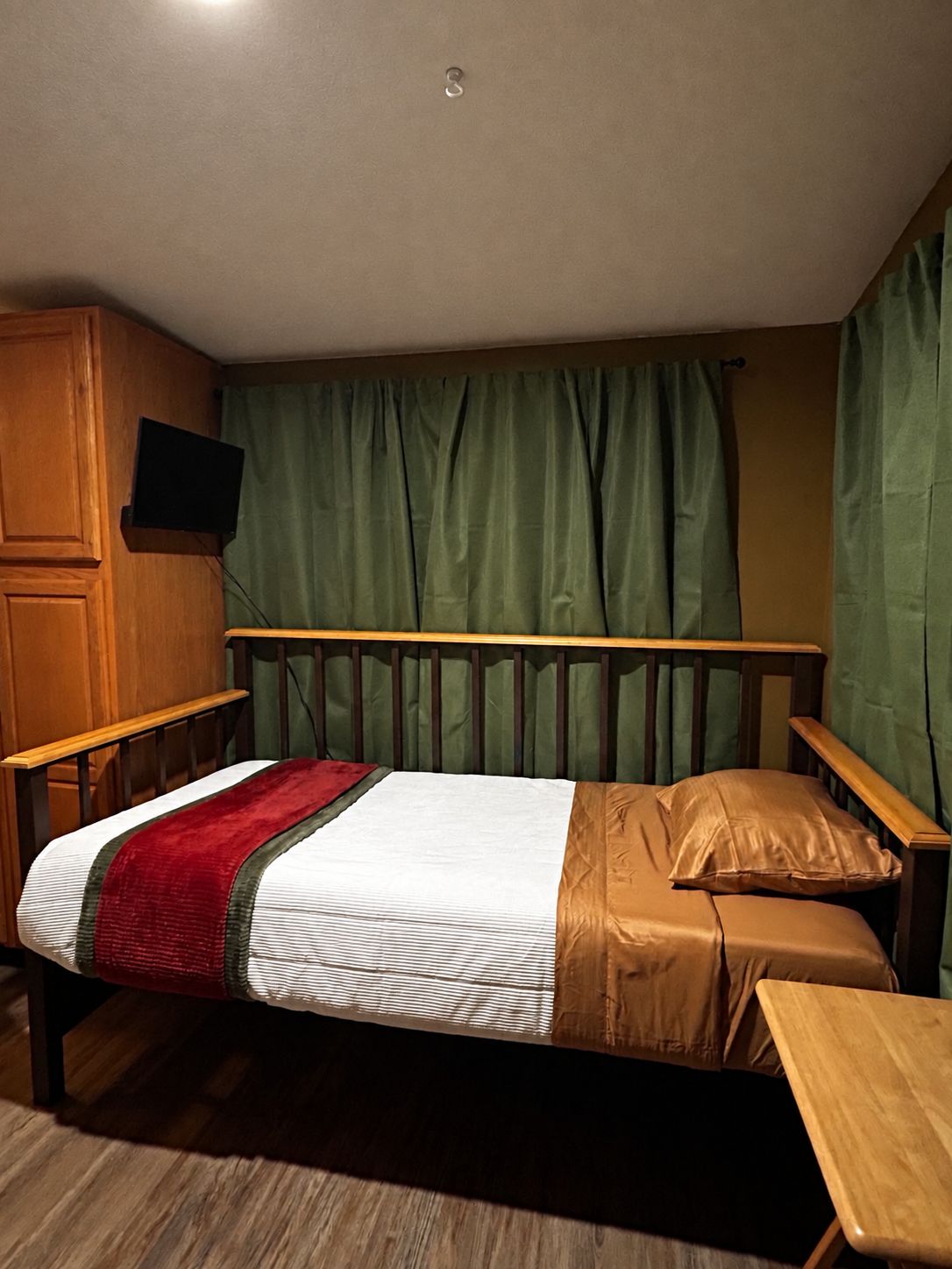 A single bed with a wooden headboard and footboard, a bedside table, and a television mounted on the wall.