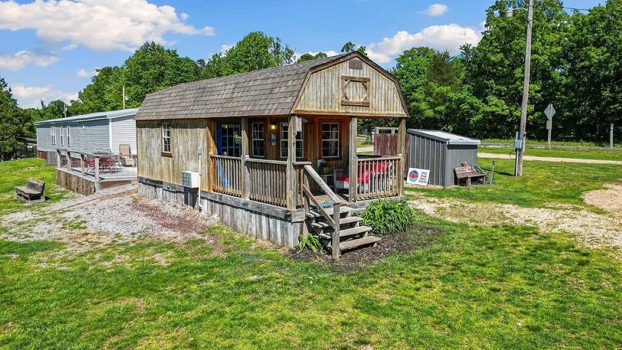 Une cabane en bois rustique, dotée d’une véranda, d’un petit abri de jardin et d’une cour gazonnée.