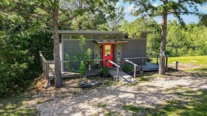 A cabin with a red door, a deck, and a fire pit.