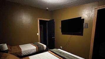 Une chambre d’hôtel avec deux lits, un téléviseur fixé au mur et un luminaire au plafond.
