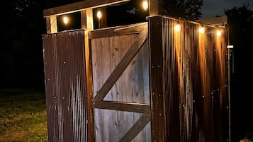 A wooden structure with a metal gate, illuminated by string lights, set on a grassy area.