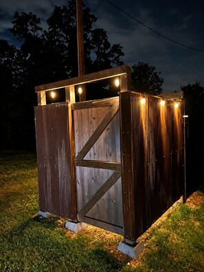 A wooden structure with a metal gate, illuminated by string lights, set on a grassy area.