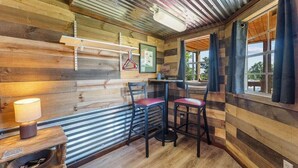 A wooden interior with a bar area, chairs, a table, and a hanging light fixture.