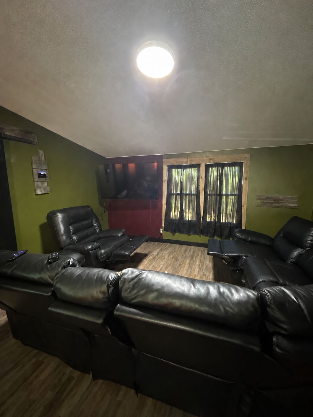 A room with a ceiling light, a window with curtains, and multiple black leather sofas.