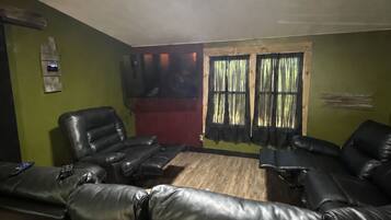 A room with a ceiling light, a window with curtains, and multiple black leather sofas.