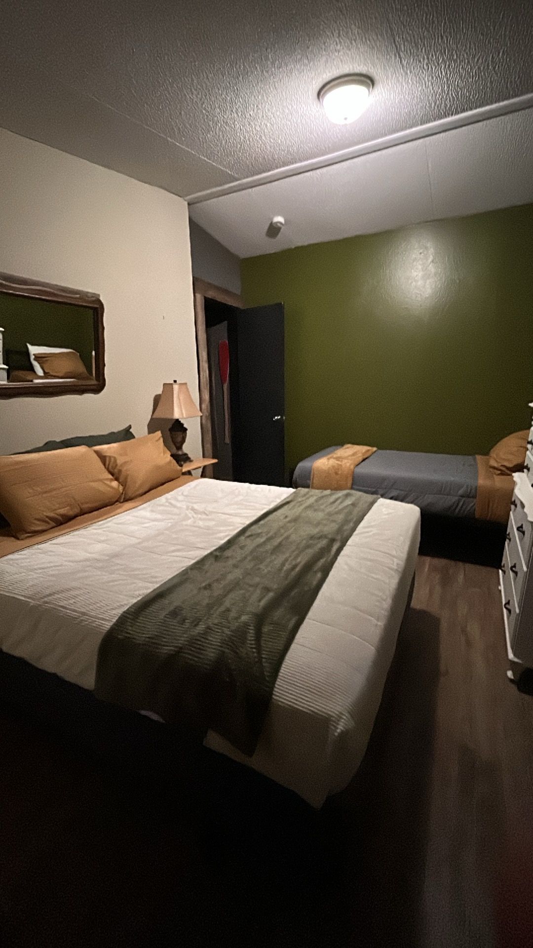 A hotel room with two beds, a nightstand, a lamp, and a green wall.