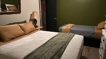 A hotel room with two beds, a nightstand, a lamp, and a green wall.