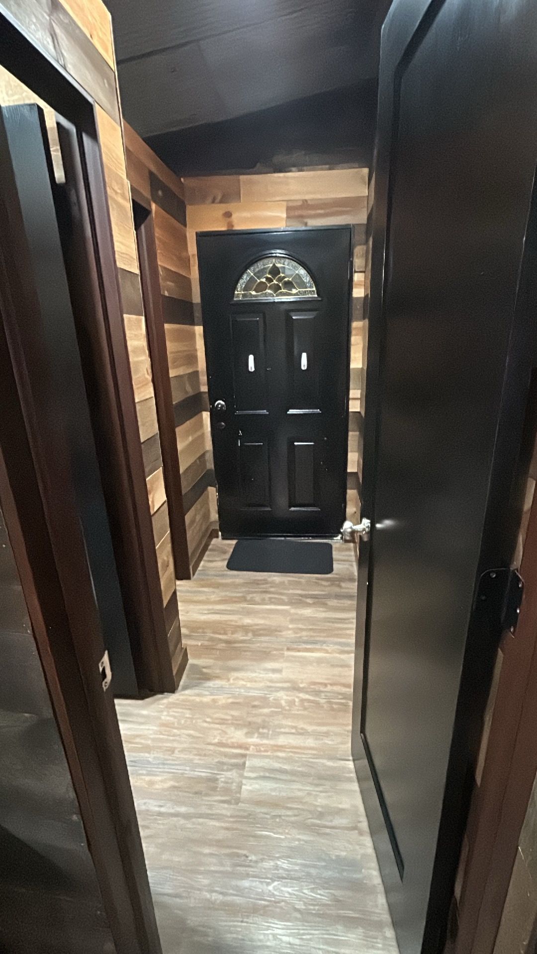 A hallway with a wooden floor leading to a black door with a glass window.