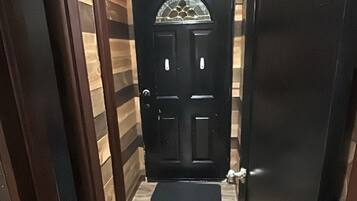 A hallway with a wooden floor leading to a black door with a glass window.