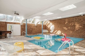 Une piscine intérieure avec un mur en briques, un piano et un ventilateur de plafond.