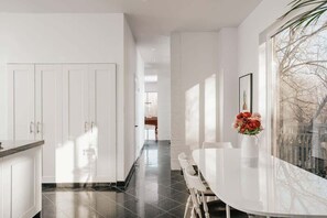 Une cuisine moderne avec des meubles blancs, un sol carrelé noir et un coin repas comprenant une table et des chaises blanches.