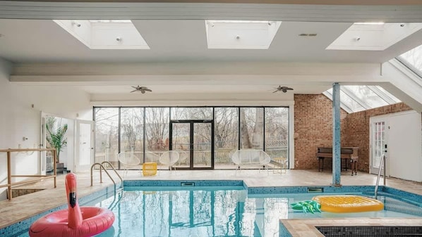 Une piscine intérieure avec des parois en verre transparent, un ventilateur de plafond et un mur en briques.