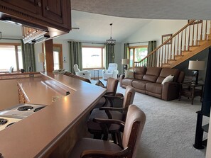 A spacious living area with a large island, a brown leather sofa, and a wooden staircase. - The "Big Easy" Waterfront Home (Huntsville)