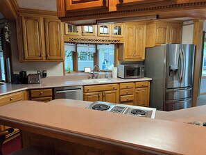 A kitchen with wooden cabinets, a stainless steel refrigerator, a microwave, and a built-in stove. - The "Big Easy" Waterfront Home (Huntsville)