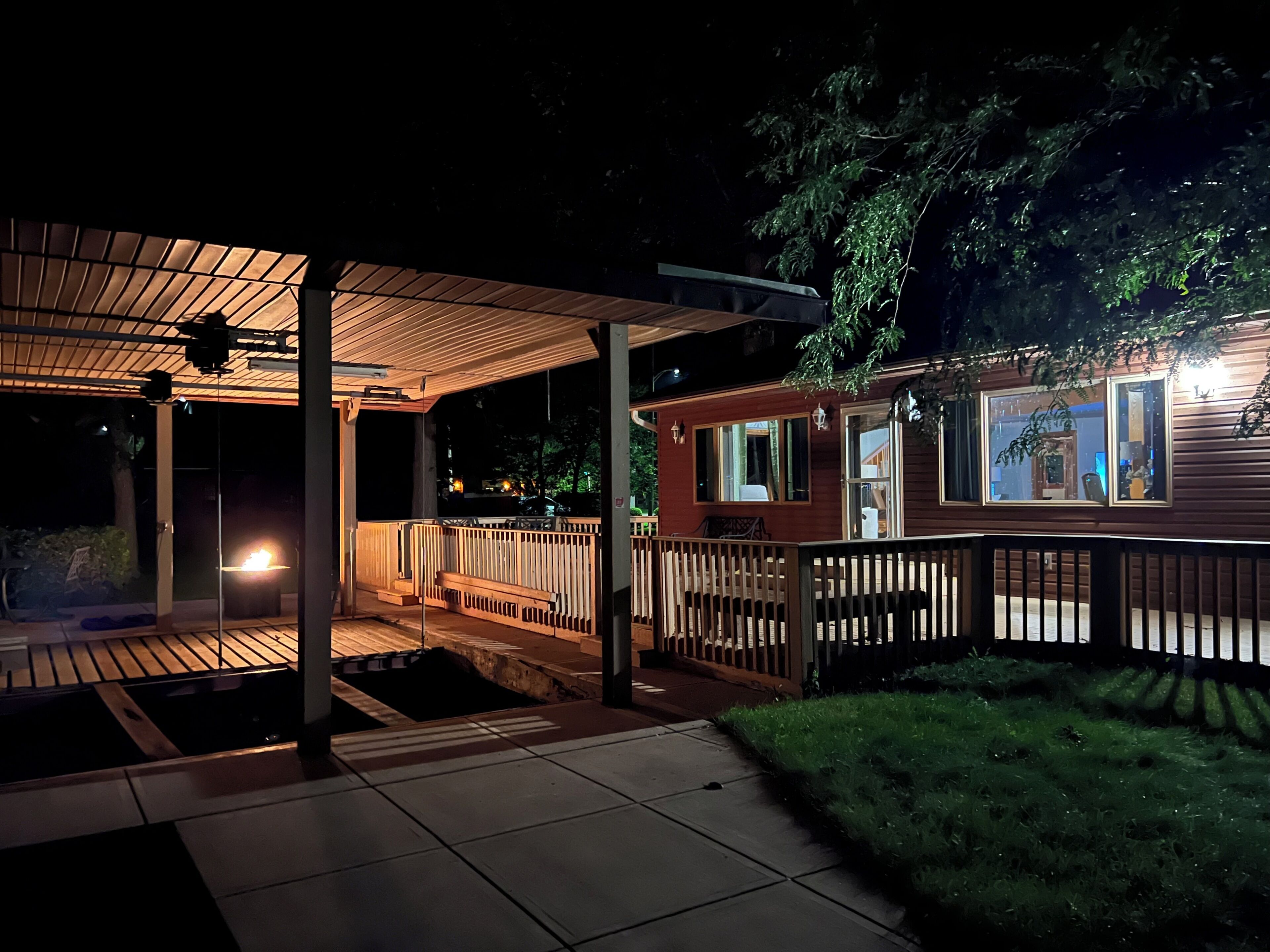 A covered outdoor area with a wooden deck, a small wooden structure with windows, and a fenced garden.