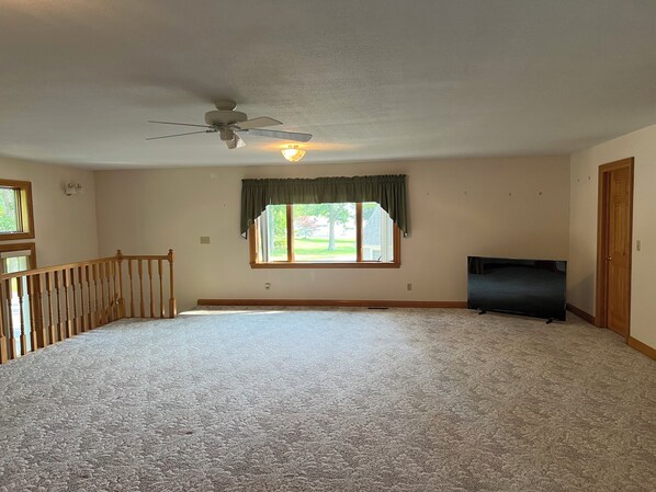 A room with a large carpeted area, a ceiling fan, a window with a view, and a door. - The "Big Easy" Waterfront Home (Huntsville)