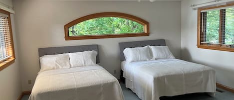 A bedroom with two beds, a ceiling fan, and a window with a view of greenery.