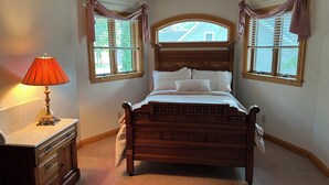 Um quarto com uma cama de madeira, uma mesa de cabeceira com abajur e duas janelas com cortinas.