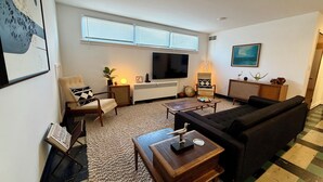 A modern living room with a flat-screen TV, comfortable seating, a coffee table, and a large window with blinds. - Lovely 2-bedroom apartment in Anchorage perfect for your getaway (Anchorage)