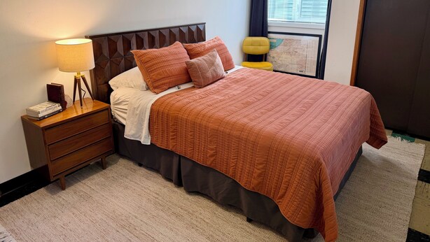 A neatly made bed with a brown quilt, a bedside lamp, and a small wooden nightstand with books. - Lovely 2-bedroom apartment in Anchorage perfect for your getaway (Anchorage)