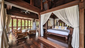 A spacious room with a large bed, wooden furniture, and a view of greenery through large windows. - Nakawanna Villa (Tambon Kamala)