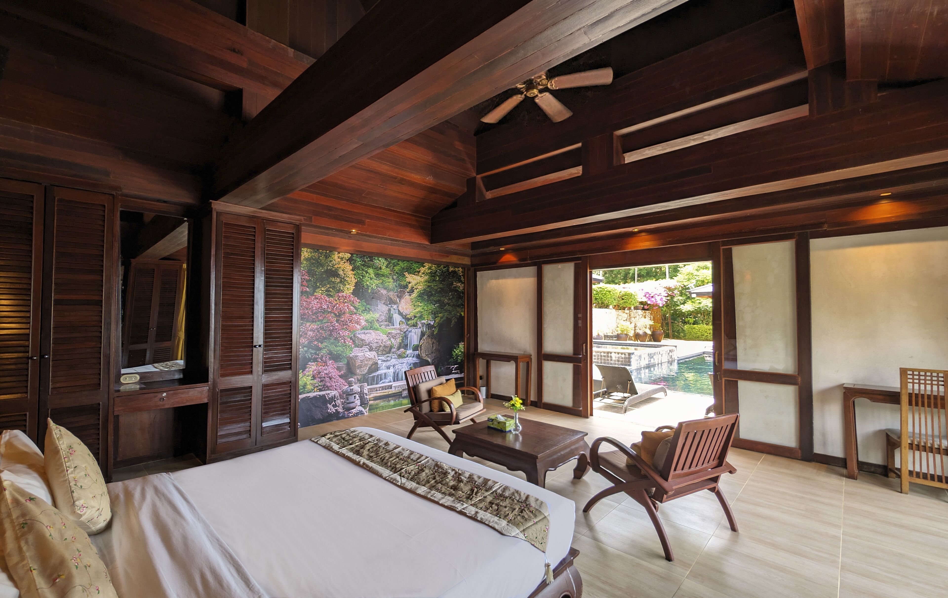 Quarto amplo com uma cama grande, um ventilador de teto e vista para um jardim através de uma porta de correr.