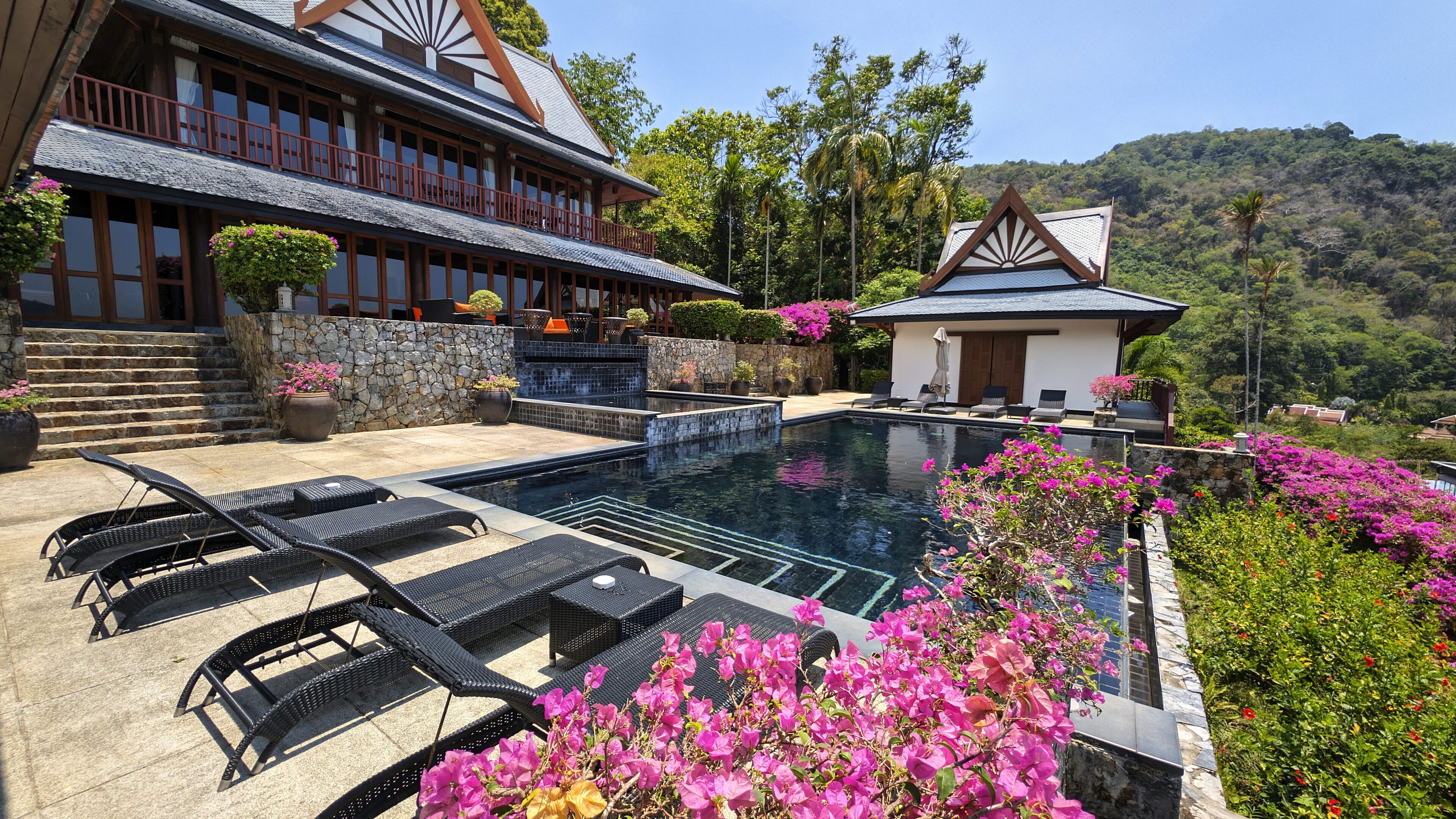 A pool area with lounge chairs, a stone wall, and a view of a hillside.