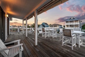 A wooden deck with white chairs and tables, overlooking a residential area with houses and a clear sky. - Jamaica Beach | Hot Tub | Canal front Dock (Jamaica Beach)