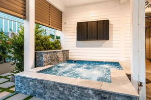 Un espace spa doté d’un jacuzzi, de murs en pierre et offrant une vue sur un bâtiment à la façade bleue.