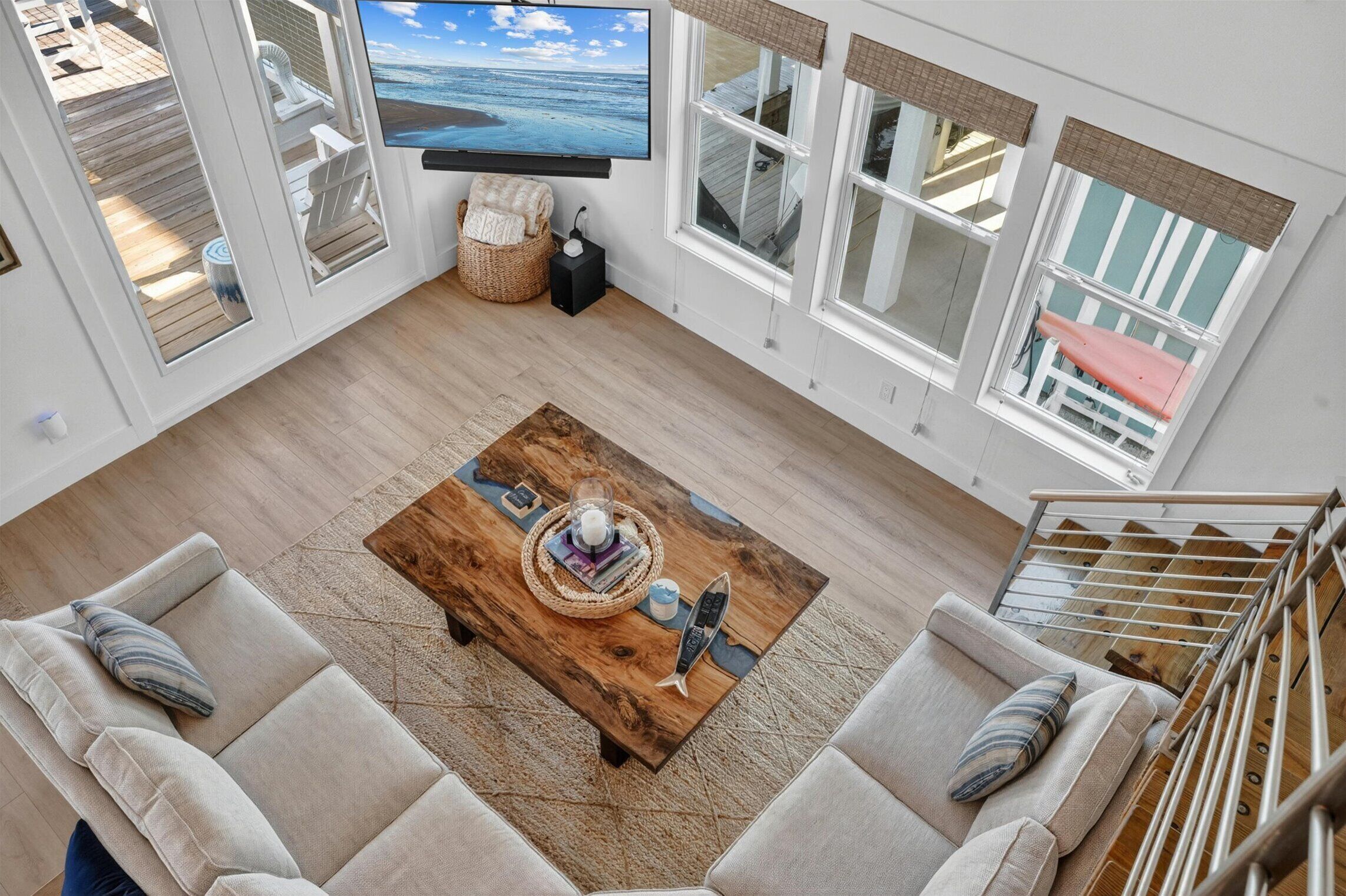 Overhead living room view with large TV, sofas, wood coffee table, and bright coastal windows.